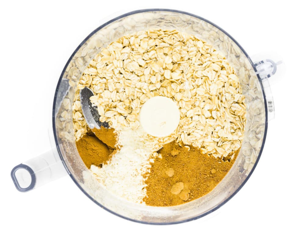 Oats and other ingredients are in the bottom of a food processor bowl.
