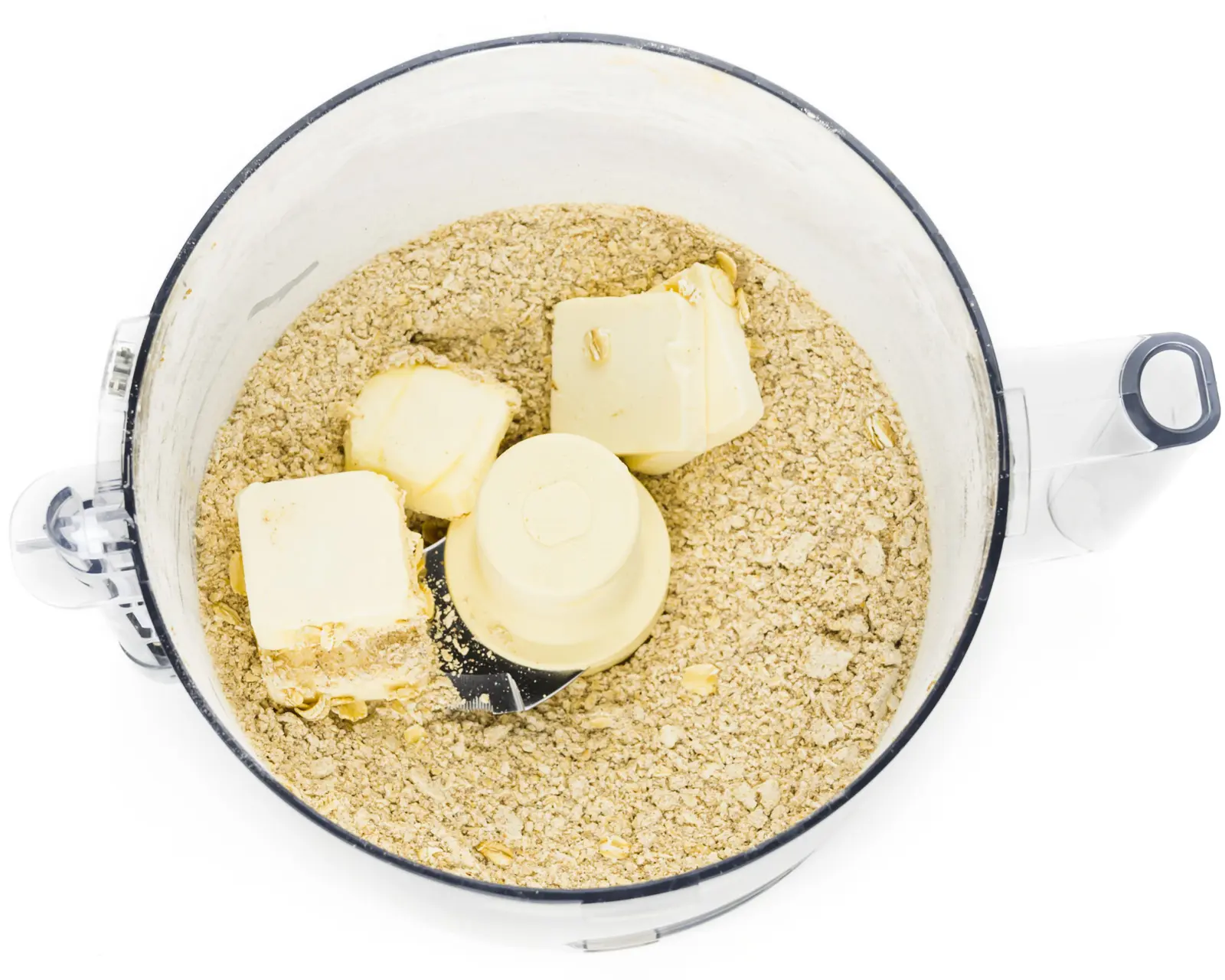 Vegan butter cubes have been added to an oat flour mixture in a food processor.