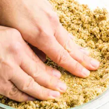 Hands are pressing an oatmeal mixture into a pie pan.