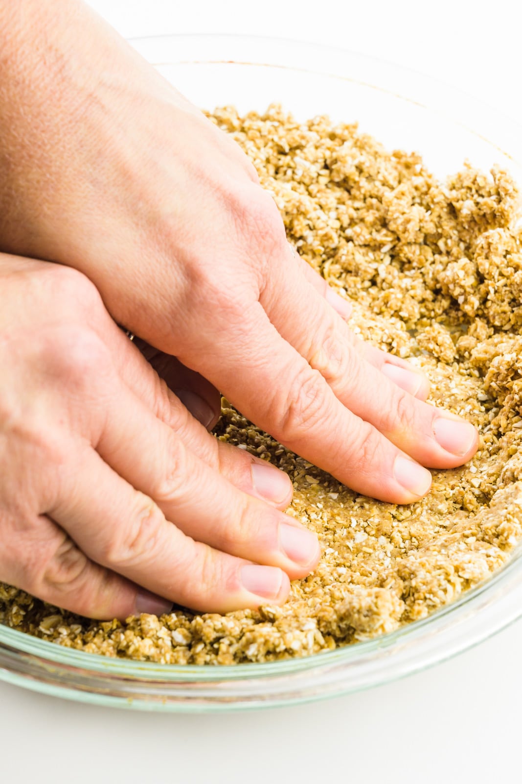 Hands are pressing an oatmeal mixture into a pie pan.