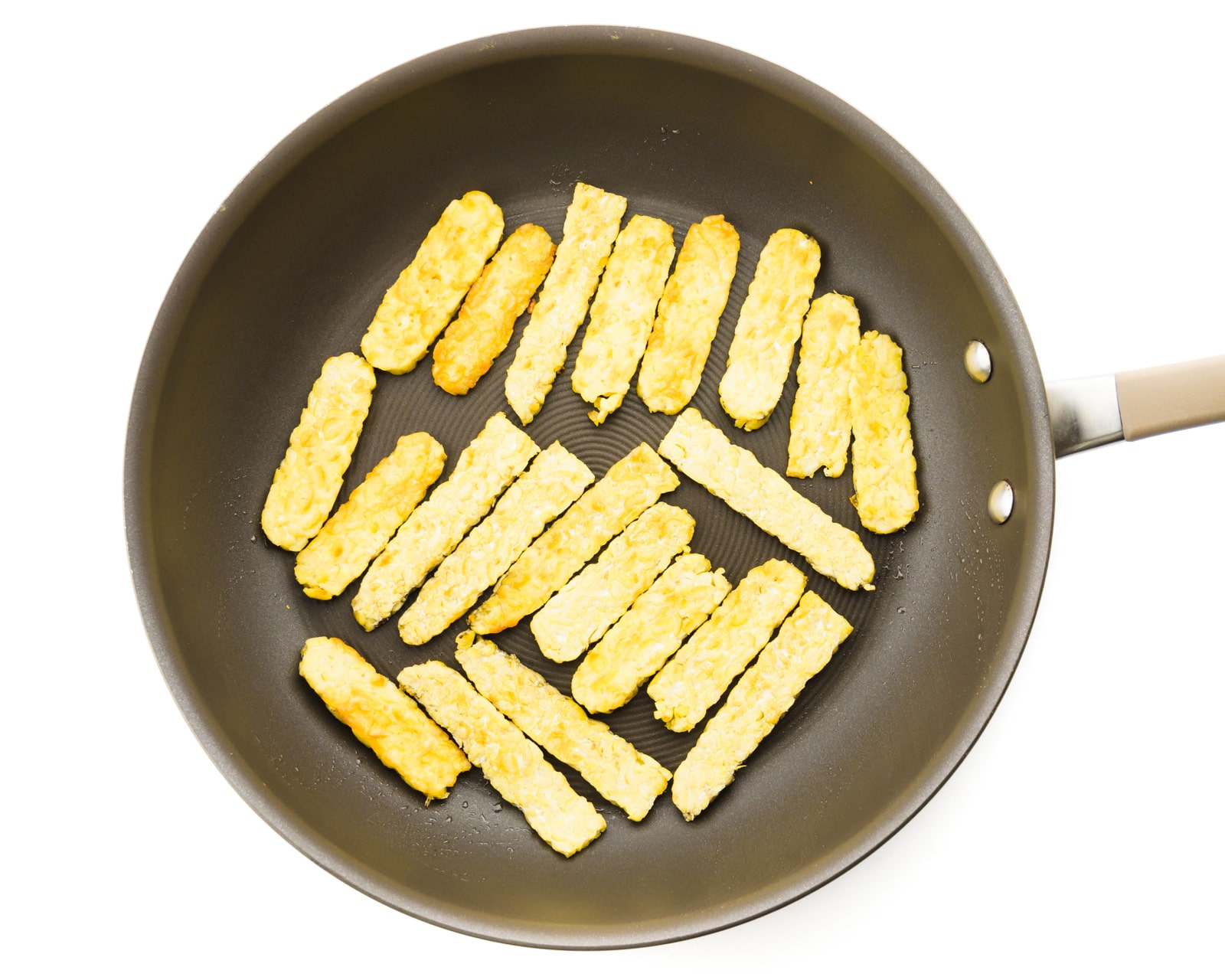 Strips of tempeh are in a skillet being cooked.