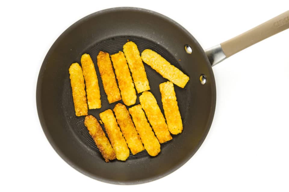 Strips of tempeh are in the bottom of a skillet.