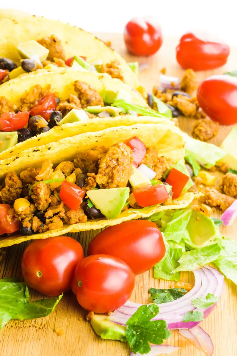 Vegan tacos are stacked next to each other with shredded lettuce and cherry tomatoes nearby.