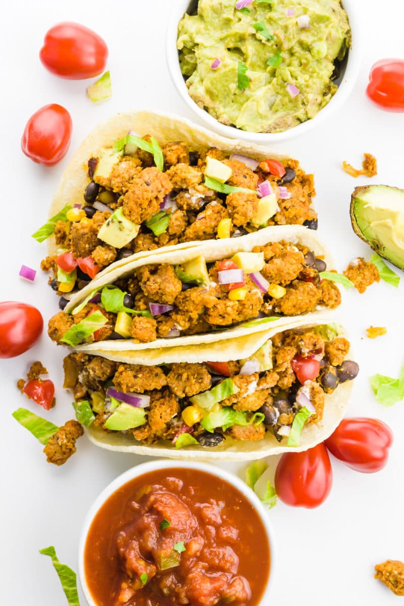 Looking down on three soft vegan tacos with lots of taco ingredients around them.