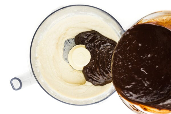 Melted chocolate is being poured into a food processor bowl.