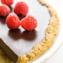 A chocolate pie with an oatmeal pie crust has several raspberries on top.