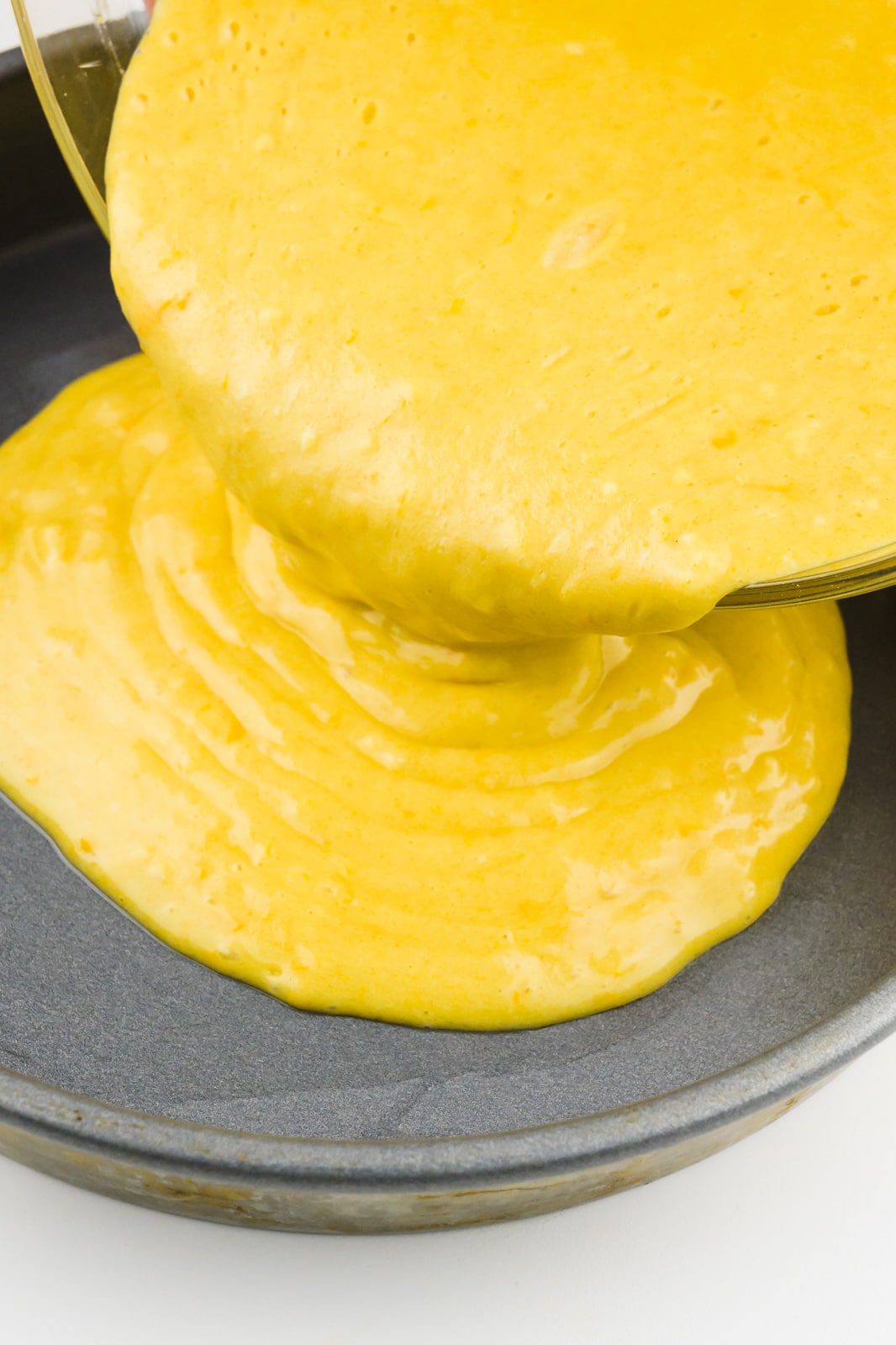 Orange cake batter is being poured into a cake pan.