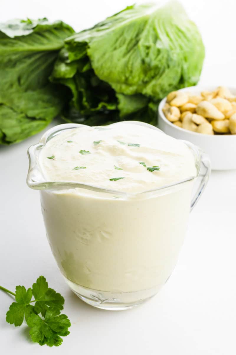 A serving dish holds vegan caesar dressing. There's lettuce and cashews behind it.