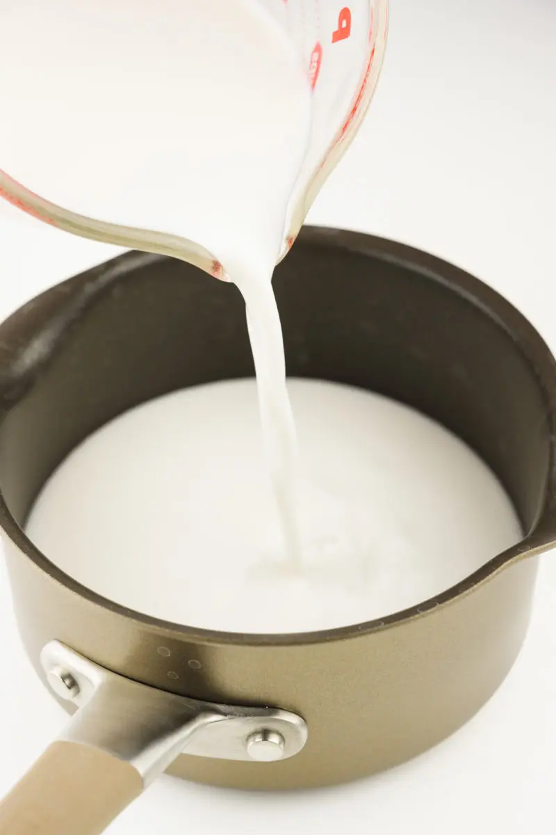 Plant-based milk is being poured into a saucepan.