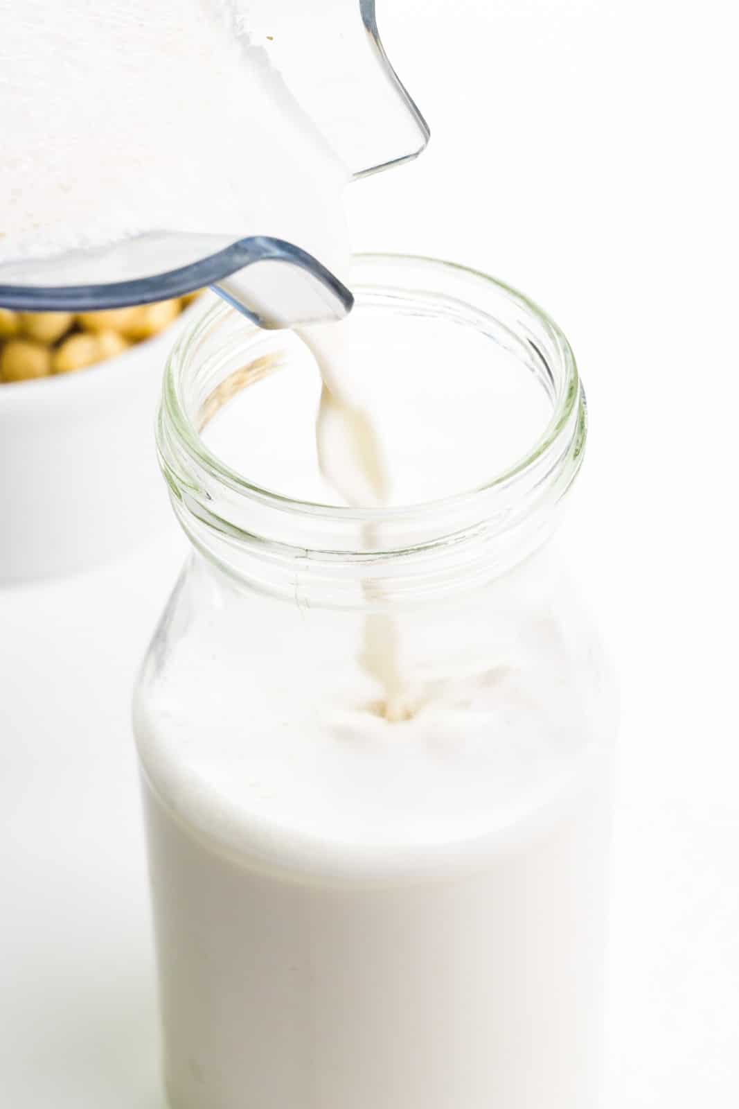 Cashew milk is being poured into a glass jar. There's a bowl of cashews behind it.