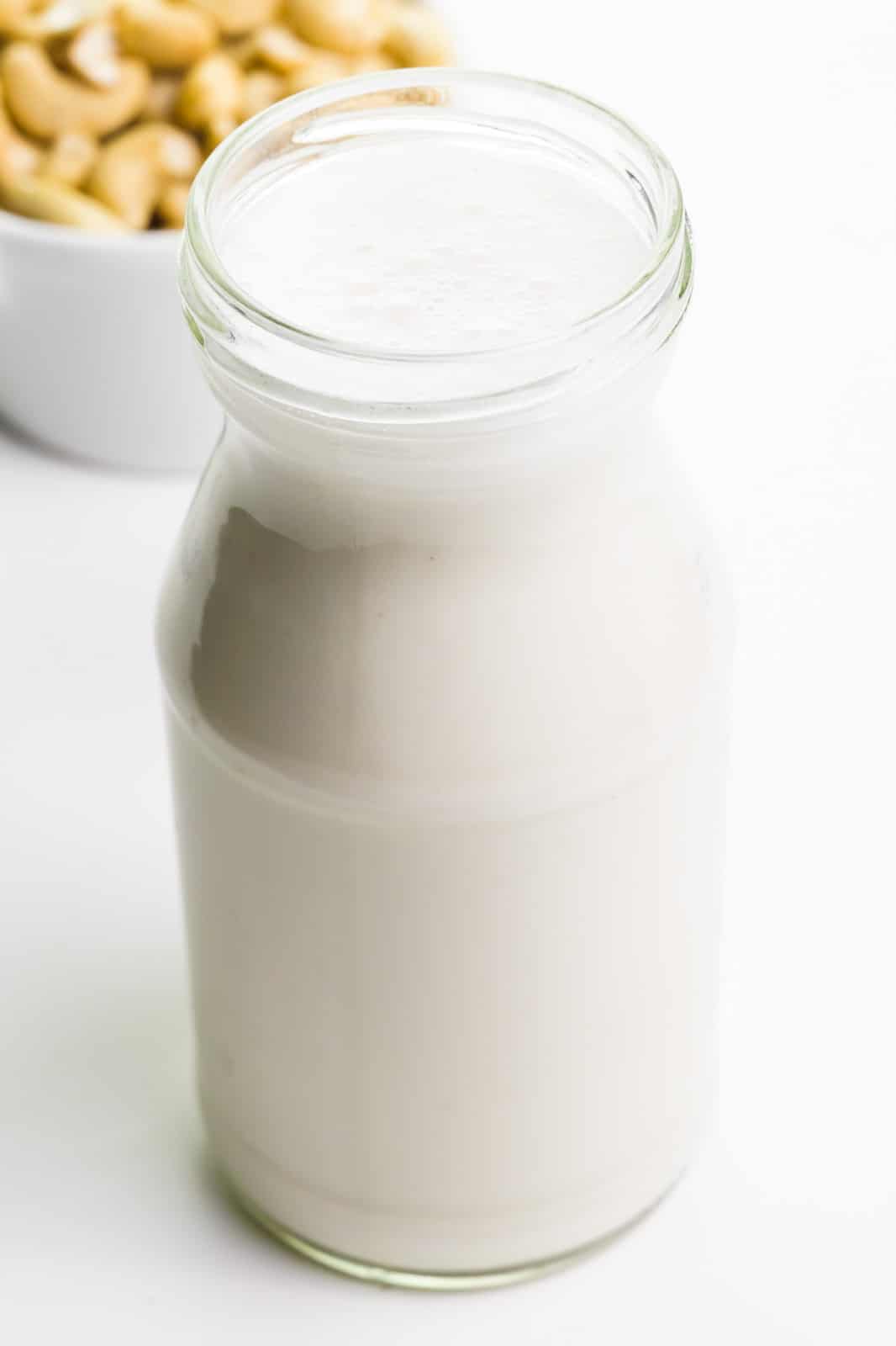 A jar holds cashew milk. A bowl of cashews is behind it.