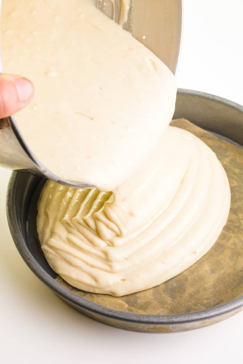 Batter is being poured into a cake pan lined with parchment paper.