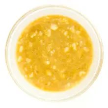 A mixture of mashed bananas and other ingredients are in the bottom of a glass bowl.