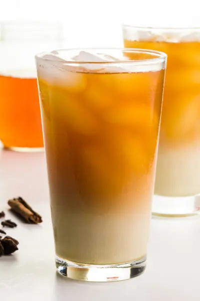A glass of iced tea with cream in the bottom, has another glass behind it, with a mason jar of concentrated tea behind it.