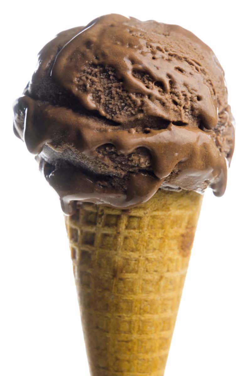 An ice cream cone holds a big scoop of vegan chocolate ice cream.