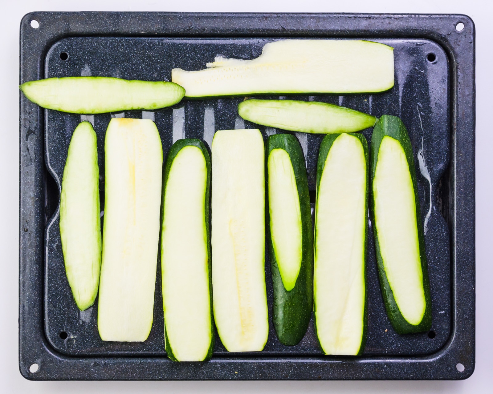 Zucchini slices are on a roasting pan.