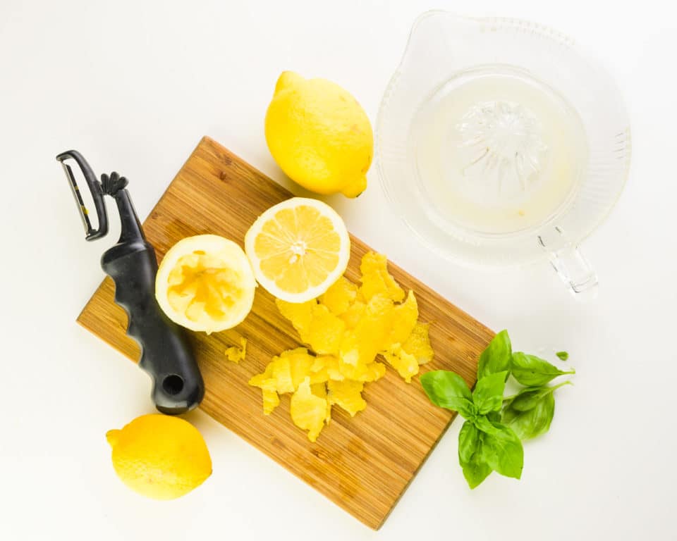 Looking down on a cutting board with cut and zested lemons. There's a vegetable peeler and a fruit juicer beside it too.