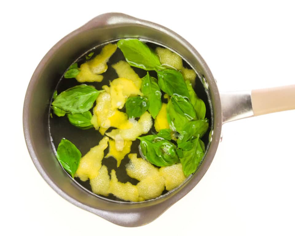 A saucepan holds liquid with lemon zest and basil leaves.