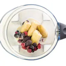 Ingredients for a smoothie, including berries, are in the bottom of a blender.