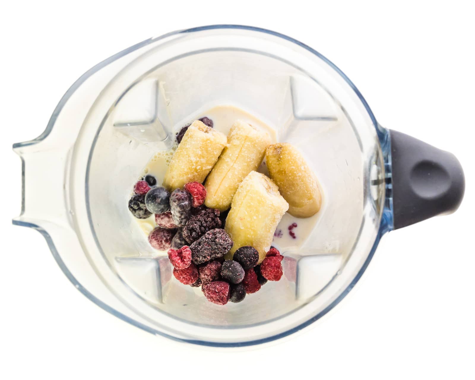 Ingredients for a smoothie, including berries, are in the bottom of a blender.