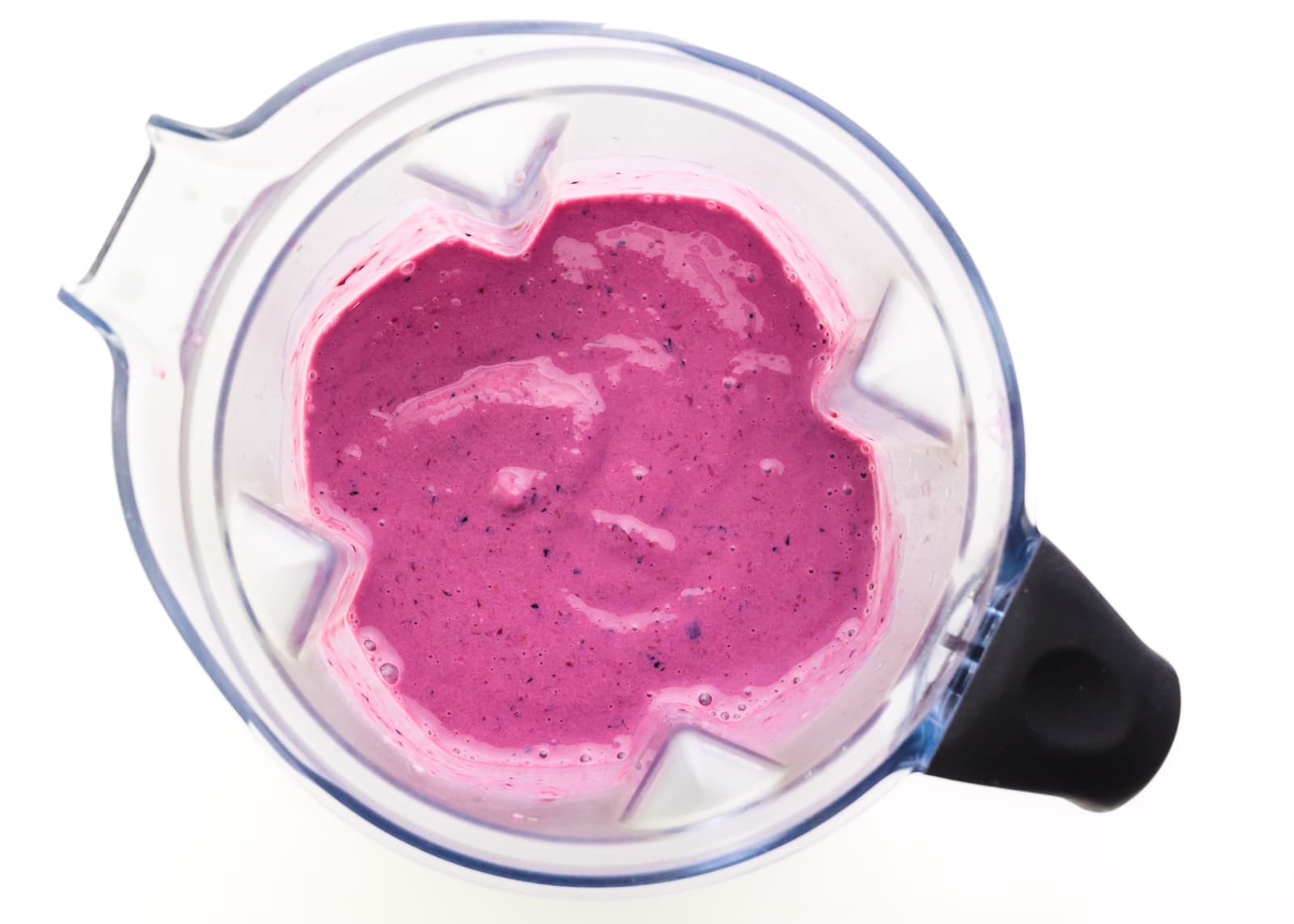 A bright pink berry mixture is in the bottom of a blender jar.