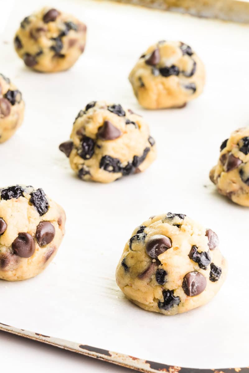 A cookie sheet is topped with parchment paper and cookie dough balls.