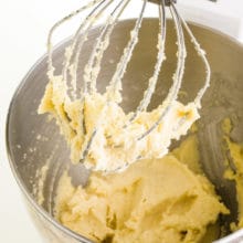 Vegan butter has been combined in a mixing bowl with sugar. The prongs of the mixer are coated with the mixture too.