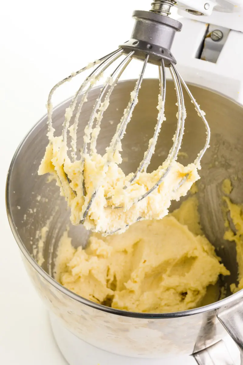 Vegan butter has been combined in a mixing bowl with sugar. The prongs of the mixer are coated with the mixture too.