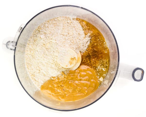 Ingredients, like flour and peanut butter, are in the bottom of a food processor bowl.