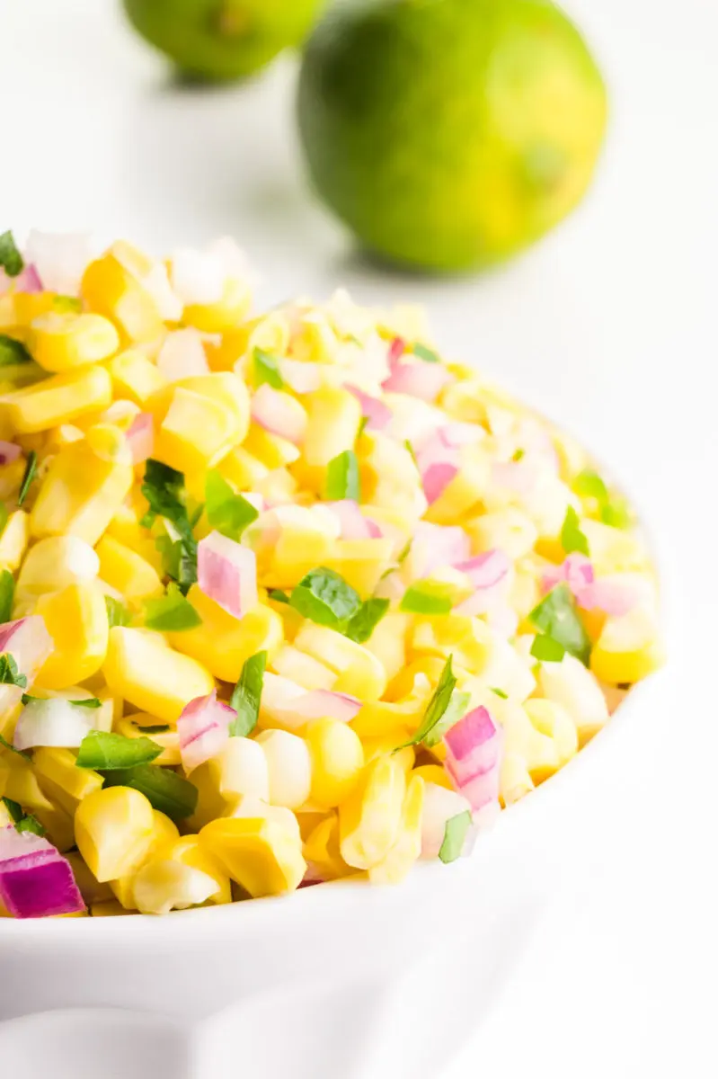 A close-up of a bowl of corn salsa with two whole limes behind it.
