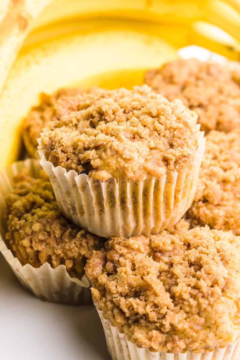 Looking down on several gluten free banana muffins with crumble topping. There are bananas behind the muffins.