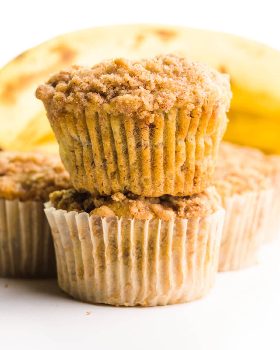 Two muffins are stacked on top of each other with more muffins and bananas behind them.