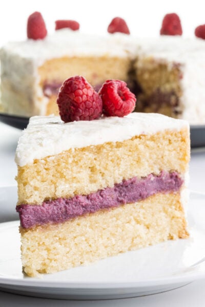 A slice of raspberry coconut cake on a plate sits in front of the rest of the cake.