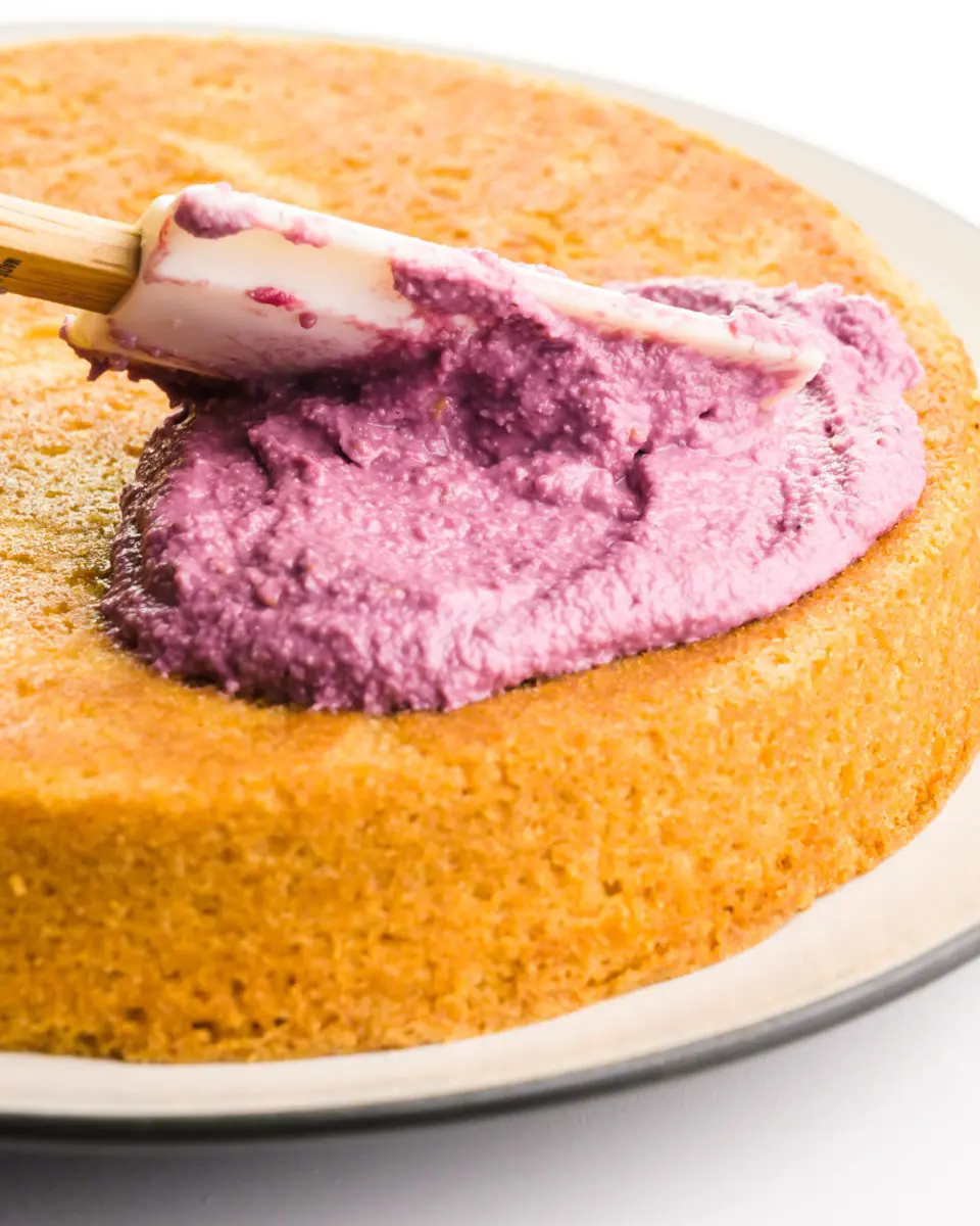 A spatula is spreading raspberry cream over a cake.