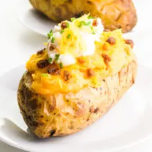 A vegan twice baked potato sits on a plate. It has vegan bacon, sour cream and cheese on top.