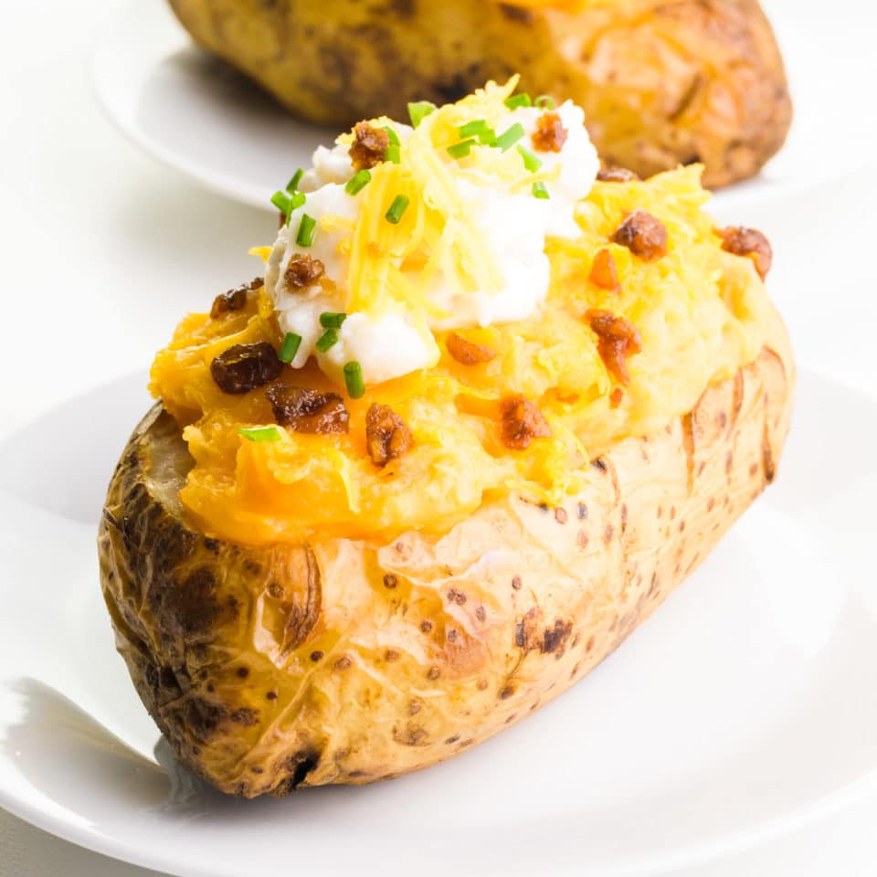 A vegan twice-baked potato sits on a plate.  It has vegan bacon, sour cream and cheese.