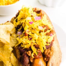 A vegan chili dog has a bowl of cheese and a bowl of chili behind it.