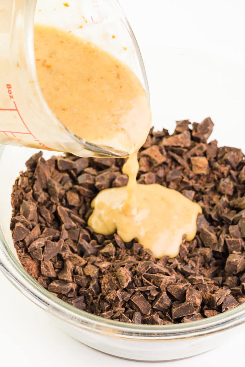A dark milk mixture is being poured over chopped up chocolate in a bowl.