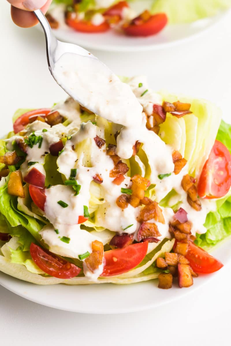 A spoon drizzles dressing over a plate with vegan wedge salad.