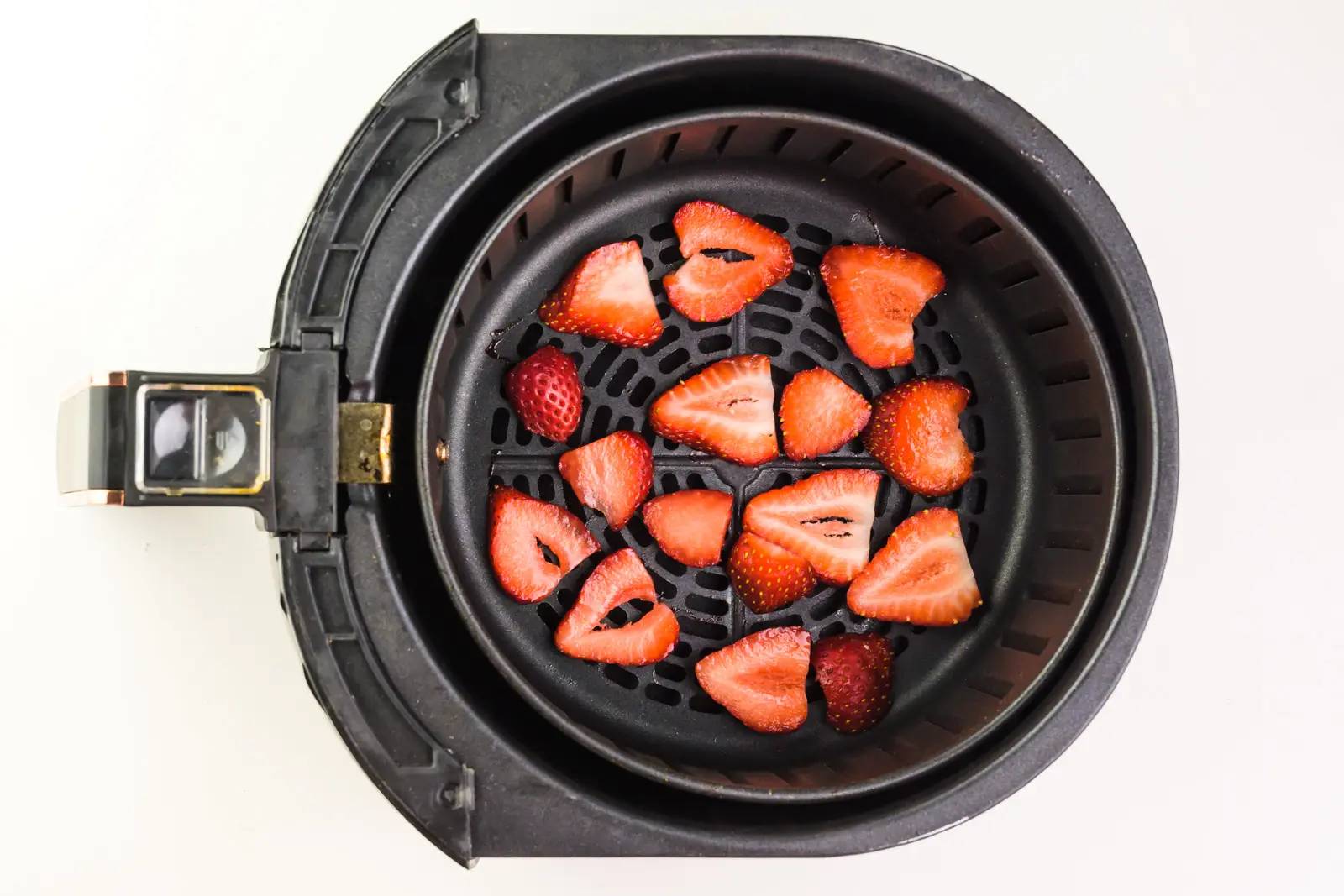 Sliced strawberries are in the bottom of an air fryer basket.
