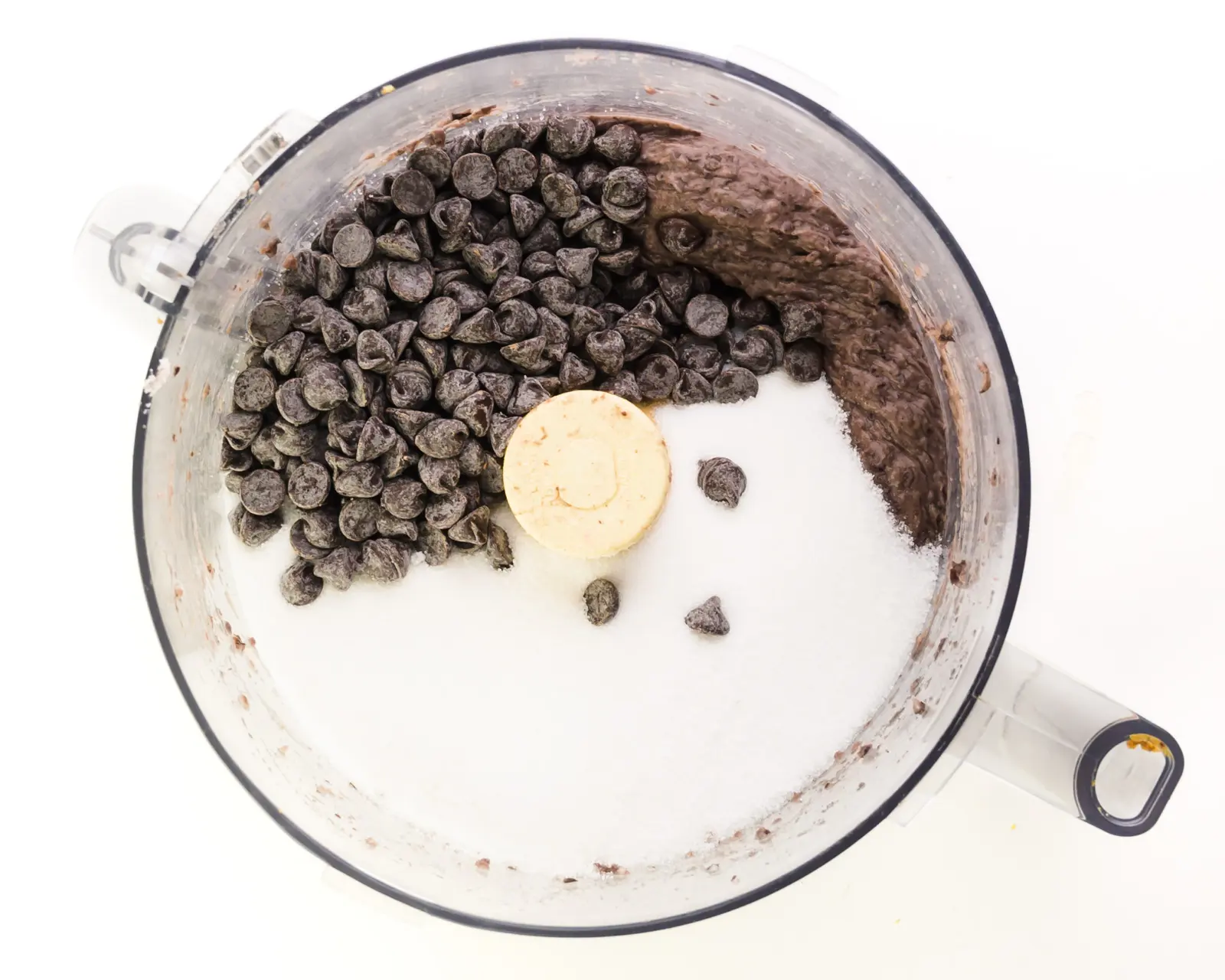 Blended black beans, chocolate chips, and sugar is in the bottom of food processor bowl.