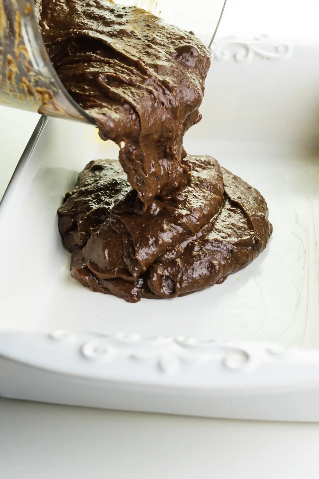 Chocolate brownie batter is being poured into a baking dish.