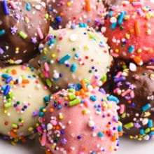Several cake balls are on a plate. They're all different colors with multi-colored sprinkles.