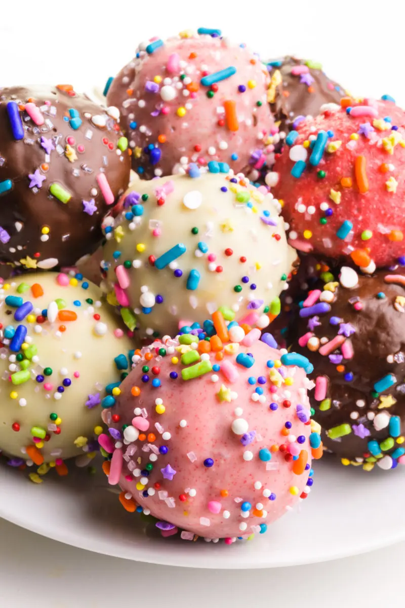 Several candy-coated balls are on a plate. They're all different colors with multi-colored sprinkles.