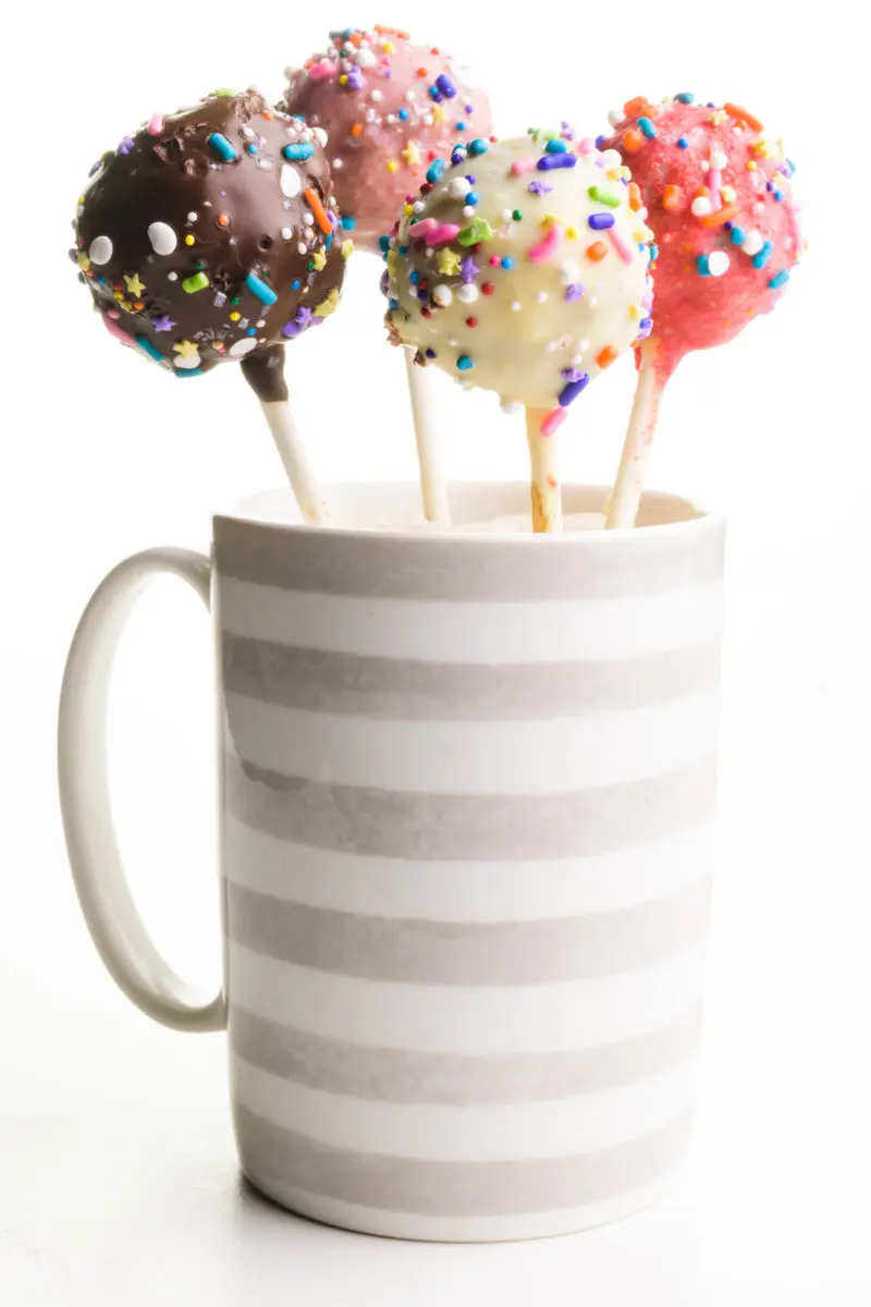 A grey and white striped coffee mug holds several cake pops.