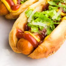A vegan hot dog bun has a vegan hot dog inside it with toppings like ketchup, mustard, and greens.