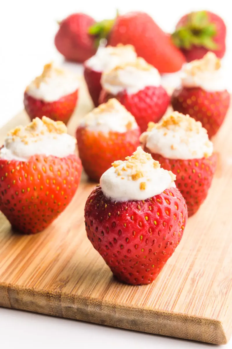 Several strawberries stuffed with cashew cream sit on a wooden cutting board.