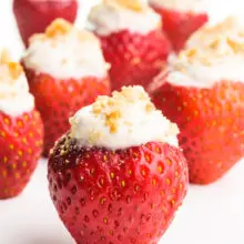 Vegan stuffed strawberries sit on a white counter. Each of them has graham cracker crumbs on top.