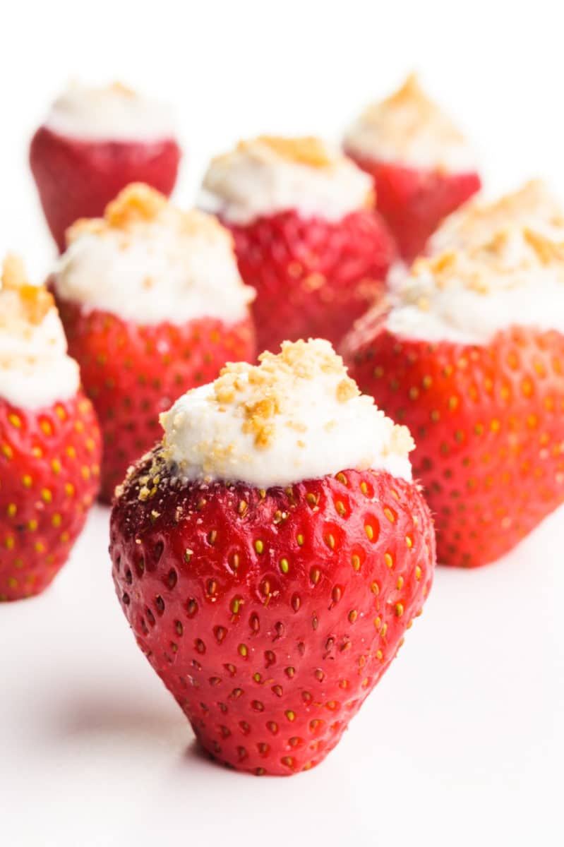 Vegan stuffed strawberries sit on a white counter. Each of them has graham cracker crumbs on top.