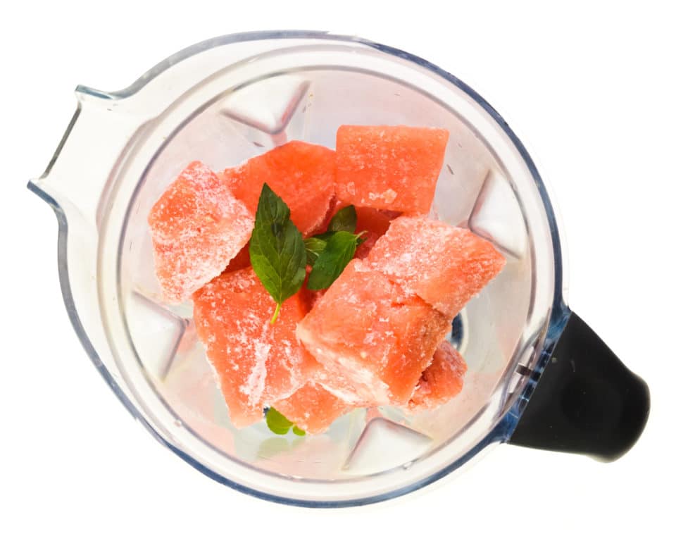 Cubes of frozen watermelon and mint are in the bottom of a blender.